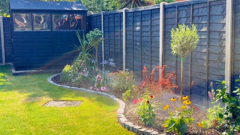 Curved planted border with granite sett edging beside a lawn, spray stakes misting the plants