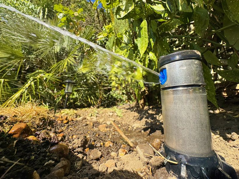 Spray stake throwing a jet of water across a planted bed
