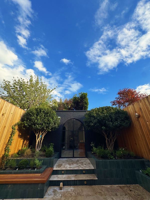 New courtyard garden with cedar cladding, green glazed-tile raised beds and two multi-stem trees either side of an arched door