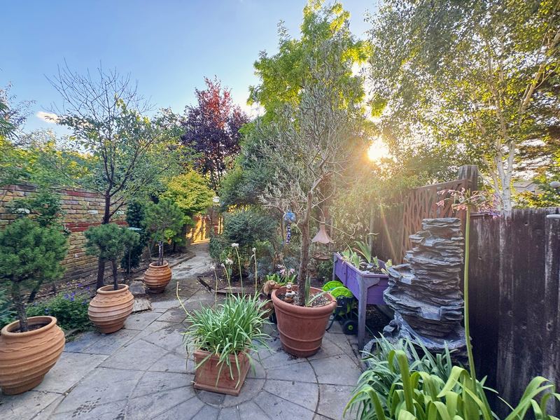 Paved courtyard garden with terracotta pots, small trees and a slate water feature in evening sun