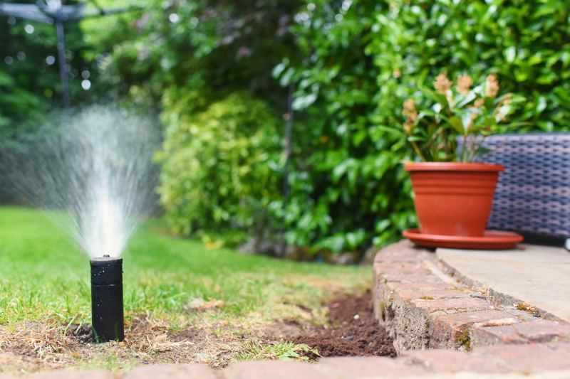 Pop-up sprinkler spraying beside a curved brick lawn edge