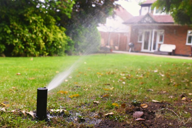 Pop-up sprinkler watering a lawn in front of a brick house